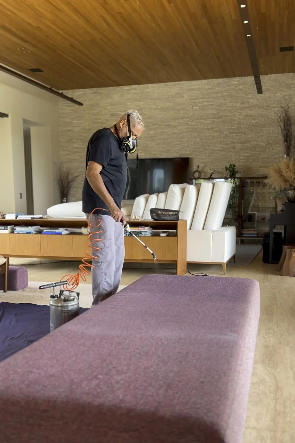 Profissional da CleanGard aplicando impermeabilizante em um estofado, com máscara de proteção