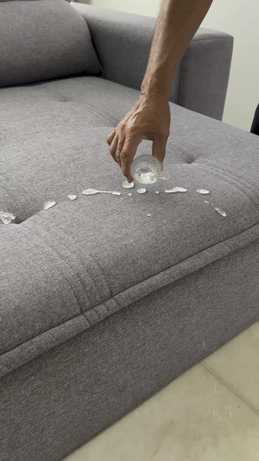 Água sendo derramada sobre sofá cinza impermeabilizado, formando gotas na superfície